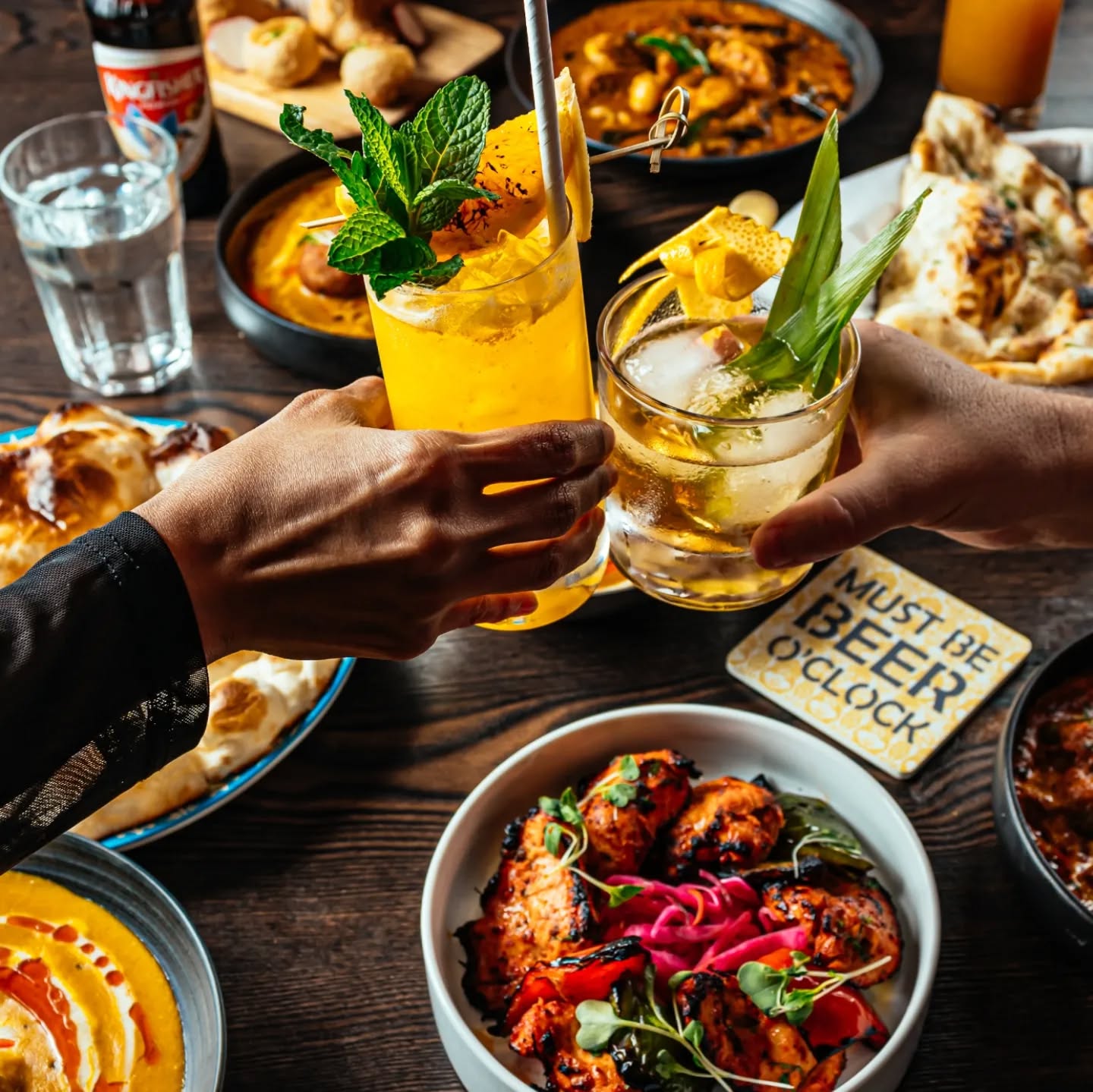 Two people toasting cocktails over a spread of Indian dishes, styled by Phototype