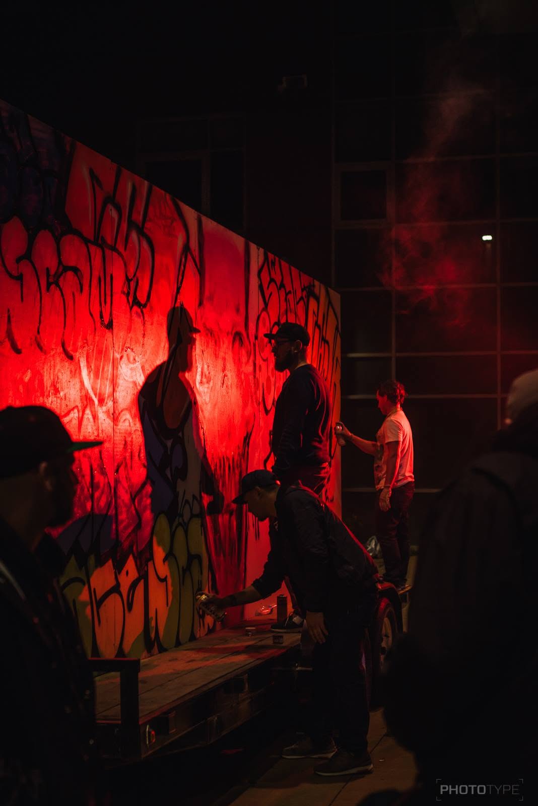Artists spray-painting a graffiti mural at night during a live event