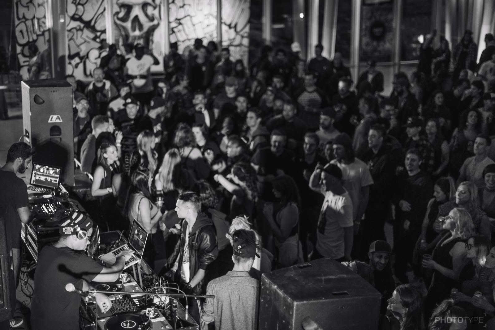 Overhead view of a packed dance floor beside the DJ booth and graffiti wall