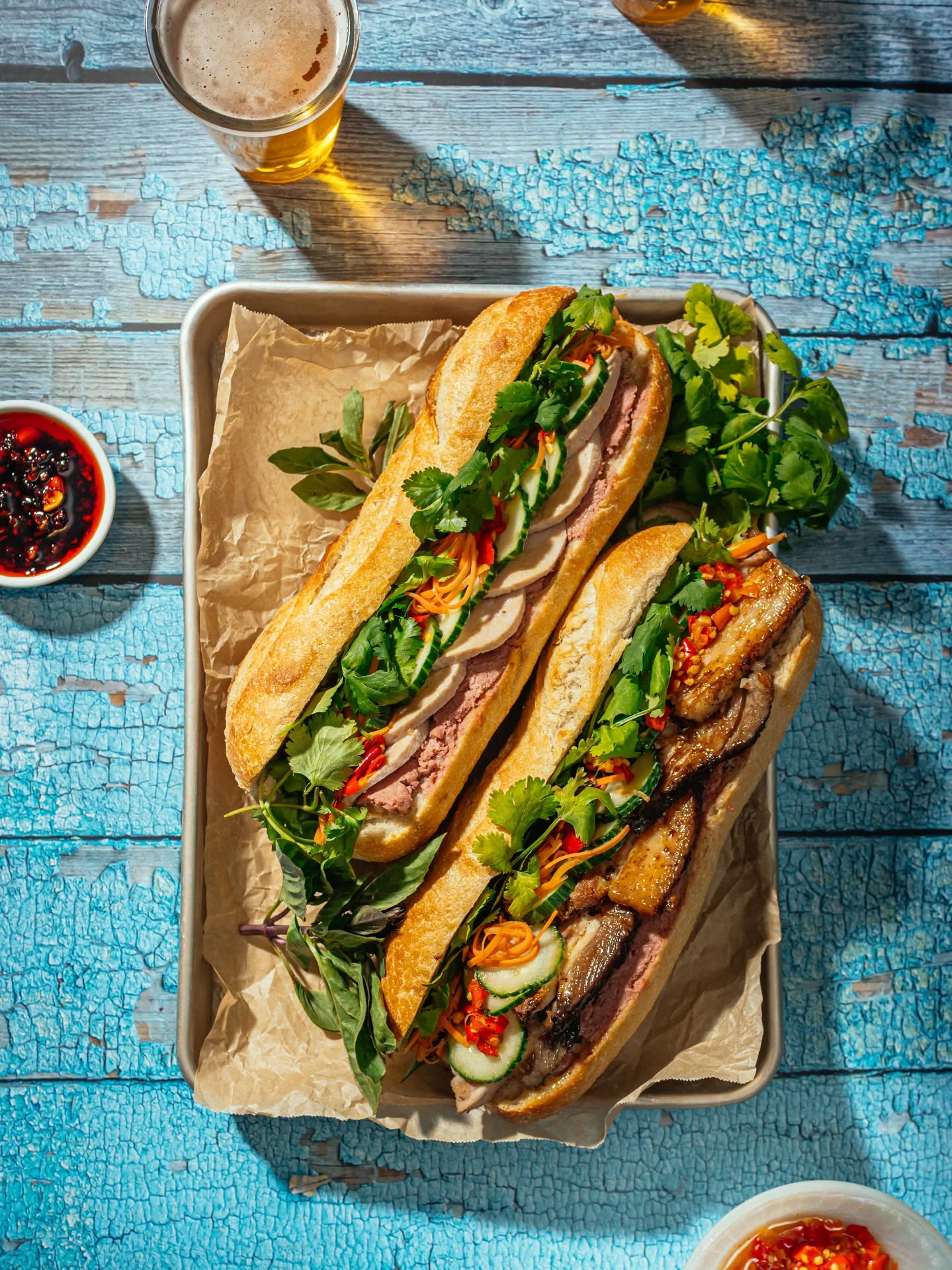 Vietnamese banh mi sandwiches on a rustic tray with a glass of beer