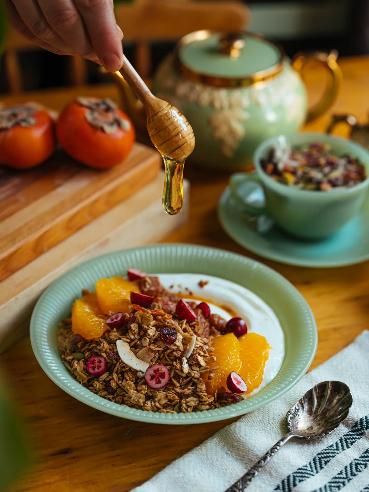 Granola and yogurt bowl with honey being drizzled over persimmons