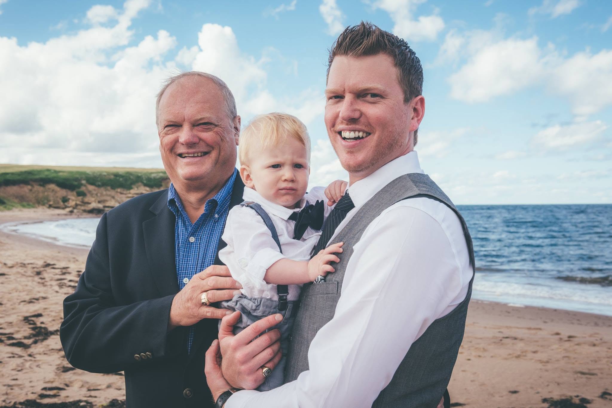 Groom holding his son alongside his father on a rocky beach
