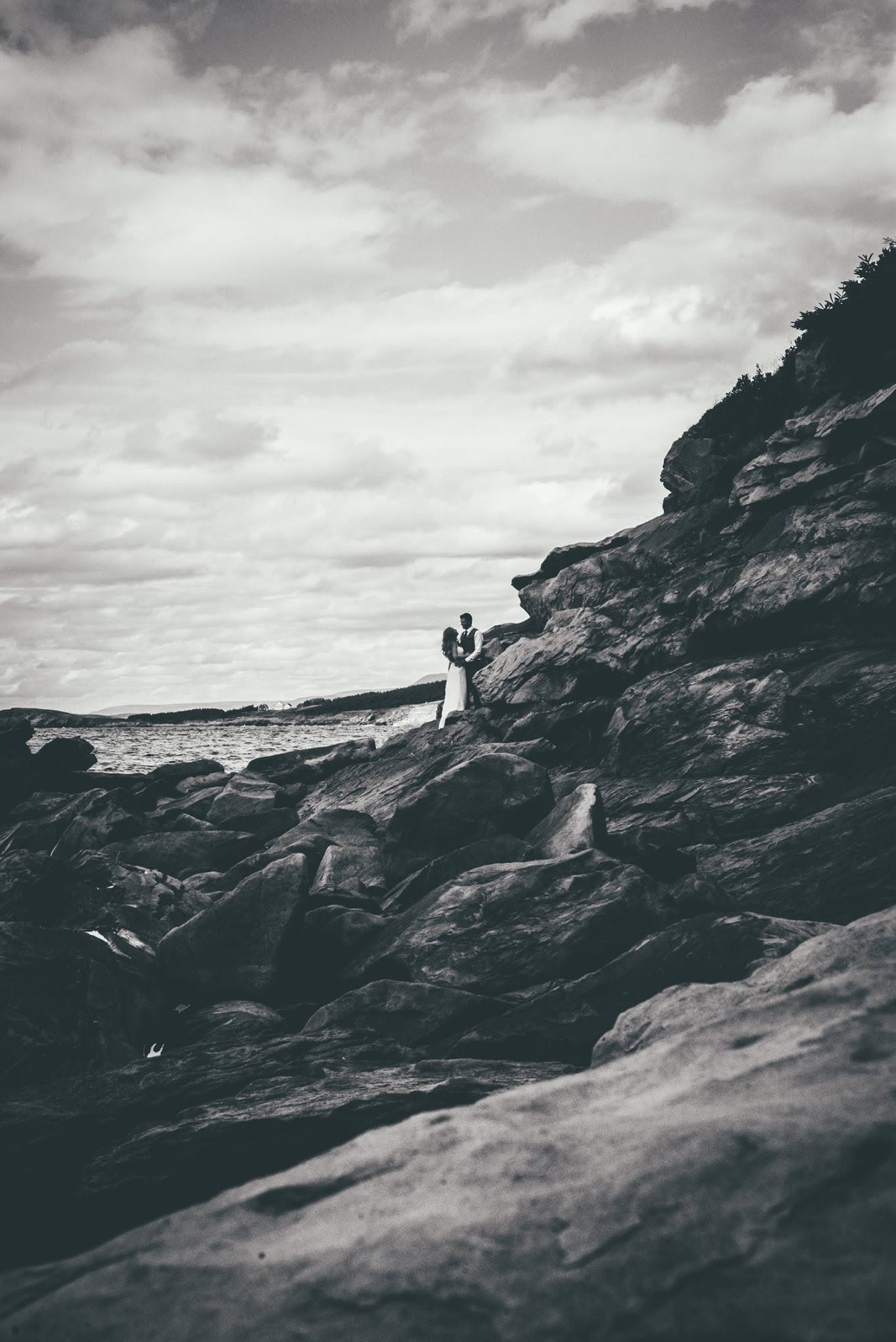 Bride and groom sharing a quiet moment on coastal rocks, black and white portrait