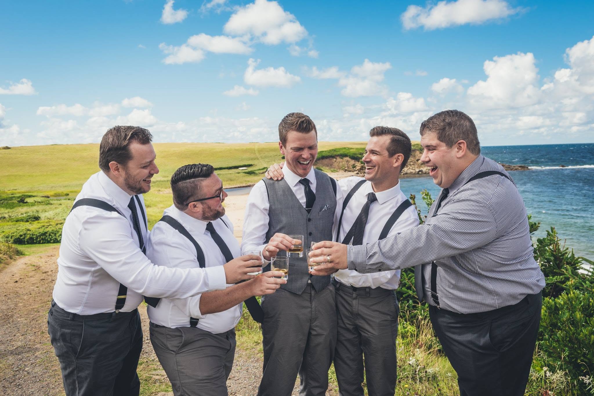Groomsmen toasting with whisky on a coastal bluff overlooking the ocean
