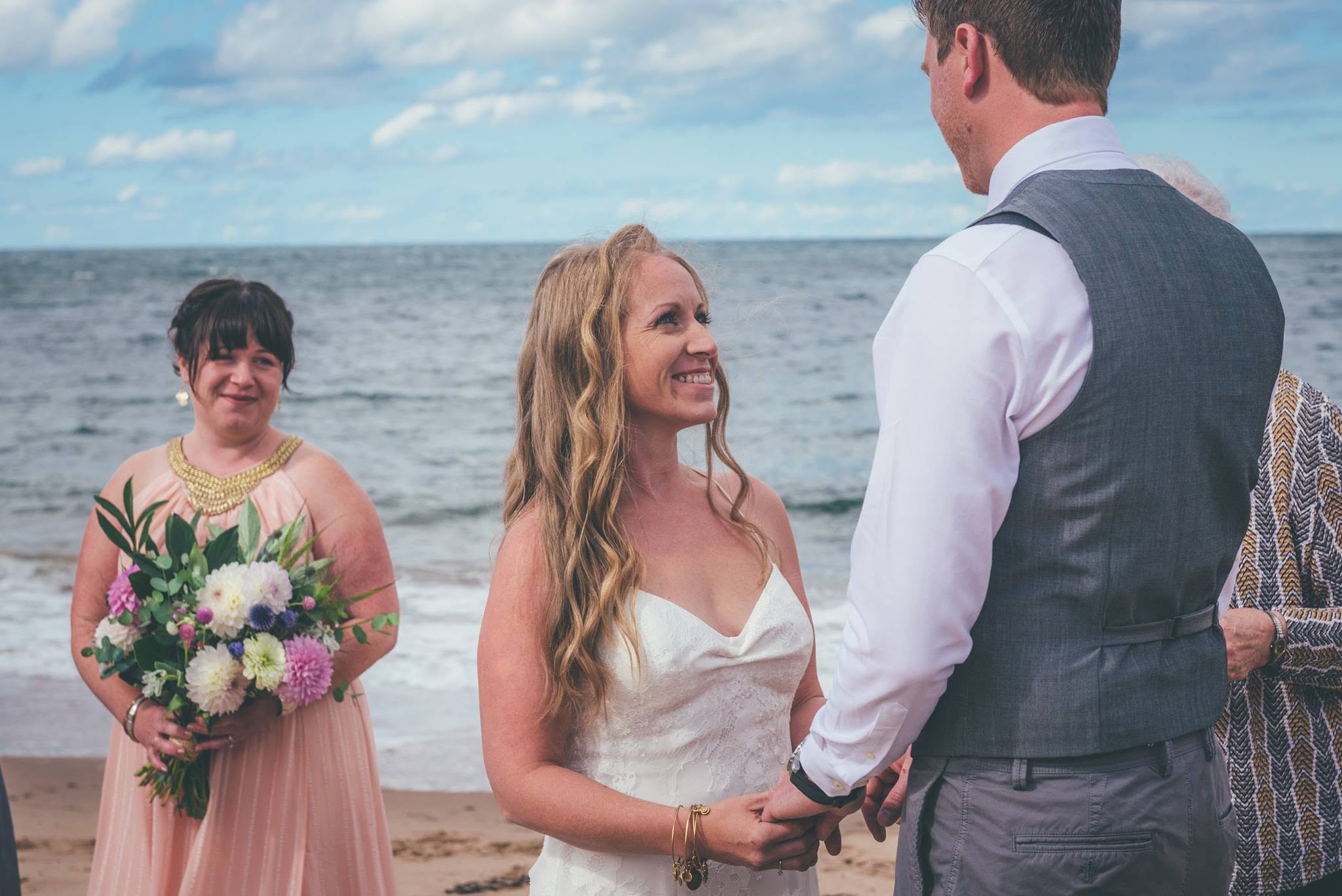 Bride and groom holding hands during their beach ceremony as a bridesmaid looks on