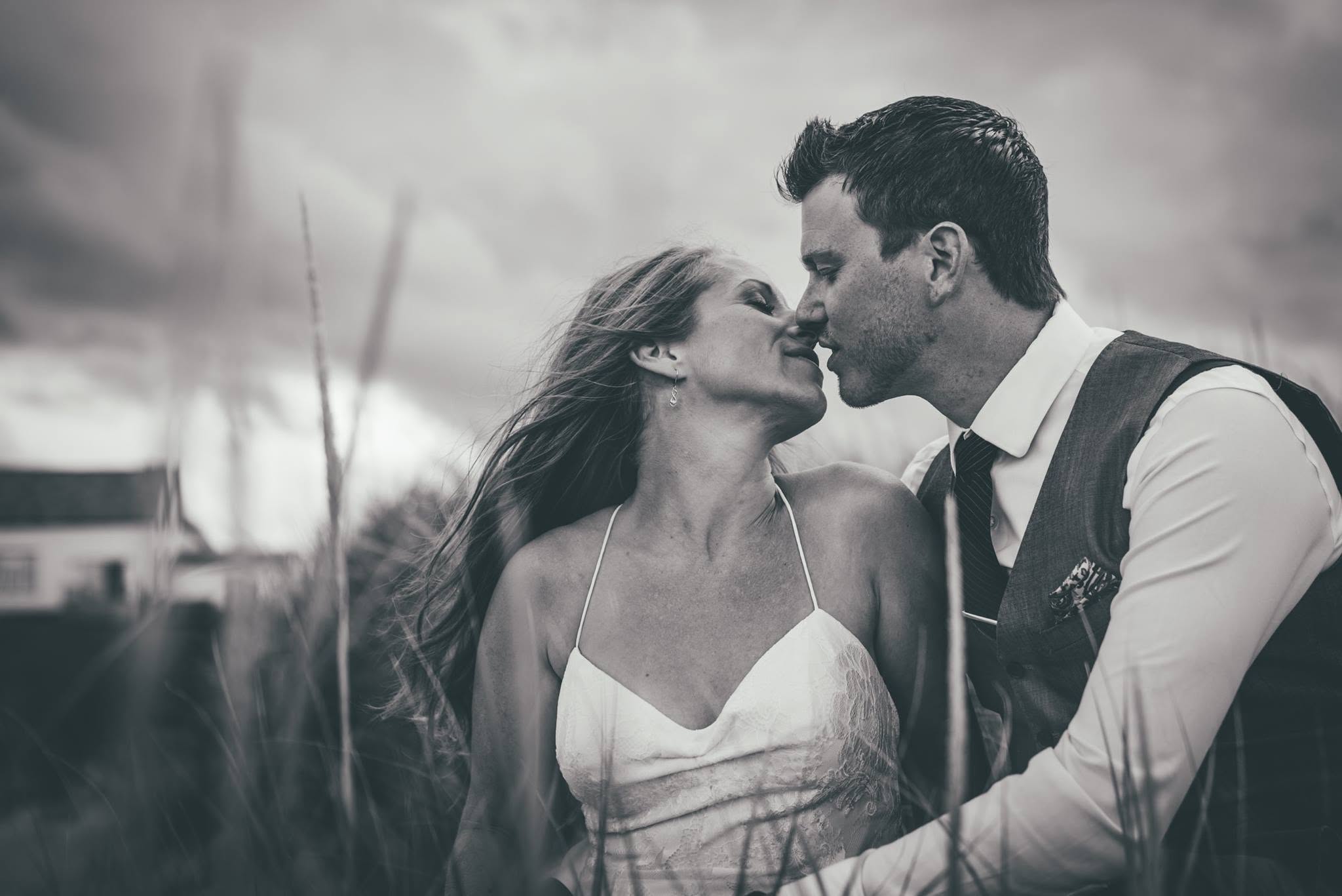 Bride and groom nose to nose in windswept grass, black and white portrait